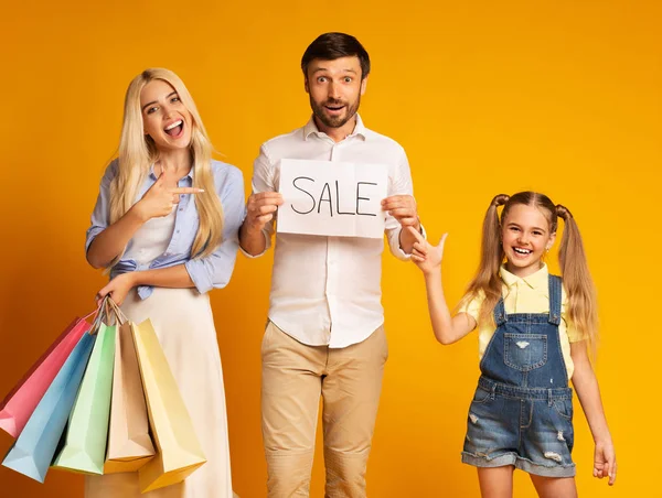 Família mostrando venda sinal segurando sacos de compras em pé no estúdio — Fotografia de Stock