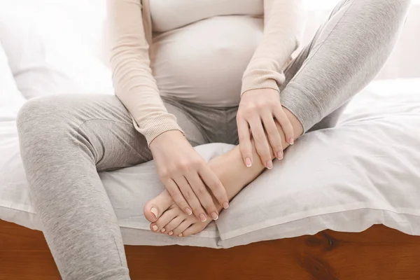 孕妇按摩她肿胀的脚坐在床上 — 图库照片