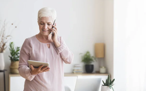 Занятая старшая женщина консультирует клиента по телефону, используя планшет — стоковое фото