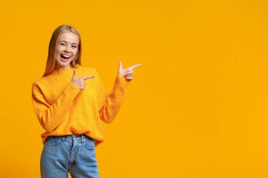 Neşeli genç kız turuncu arka plandaki fotokopi alanını işaret ediyor.