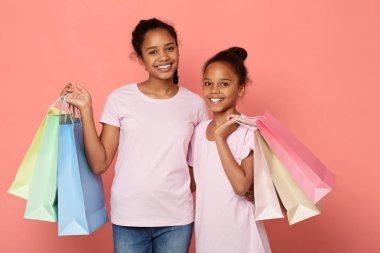 Alışveriş torbalarıyla Afrikalı kardeşler kameraya bakıyor ve gülümsüyor.