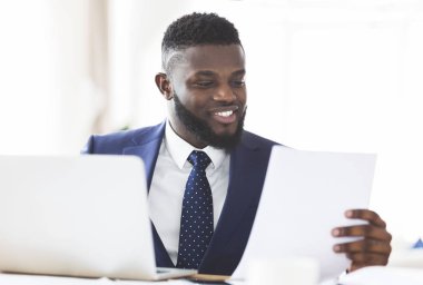 Gülümseyen Afrikalı Amerikalı iş adamı modern ofisteki raporları kontrol ediyor.