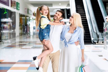 Kızını taşıyan ve alışveriş merkezinde karısına sarılan adam.