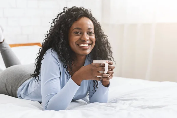Young woman relaxing on bed with cup of coffee — Stockfoto