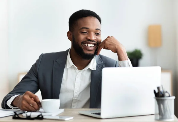 Веселий афроамериканський працівник сидить на робочому місці в сучасному офісі — стокове фото