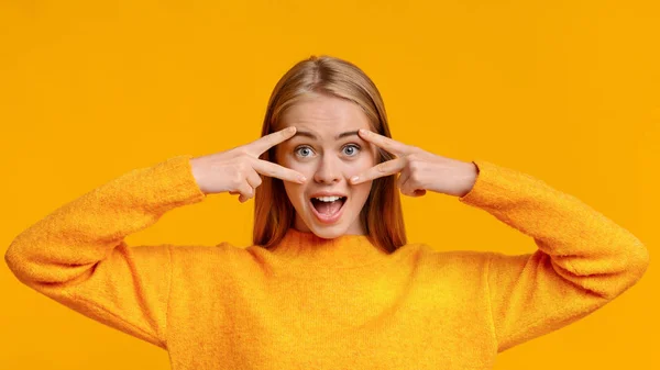 Playful teenage girl gesturing v-sign near her eyes, having fun — Stock fotografie