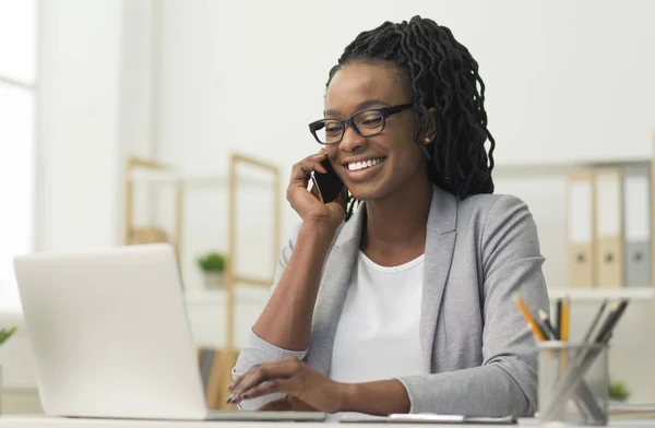 Svart ung dam som har telefon konversation sitter på arbetsplatsen — Stockfoto