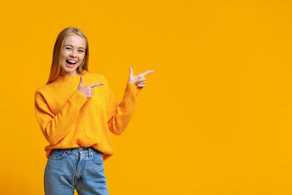 Веселая девочка-подросток, указывающая на пространство для копирования на оранжевом фоне — стоковое фото