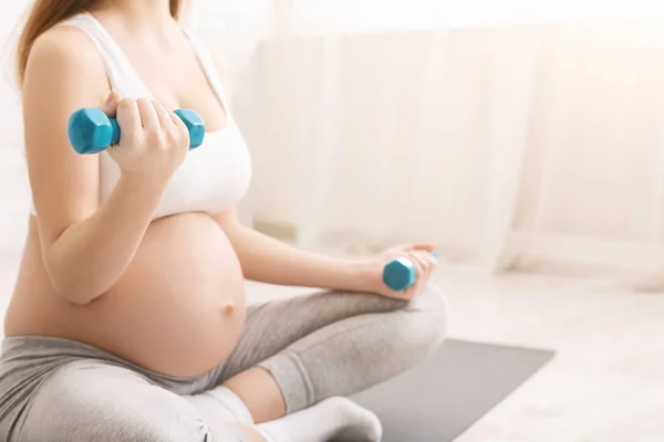 Mulher grávida levantando halteres, sentado no tapete de fitness — Fotografia de Stock