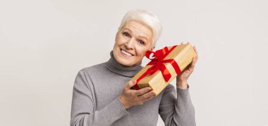 Elinde kırmızı kurdeleli hediye kutusu olan yaşlı bir kadın.