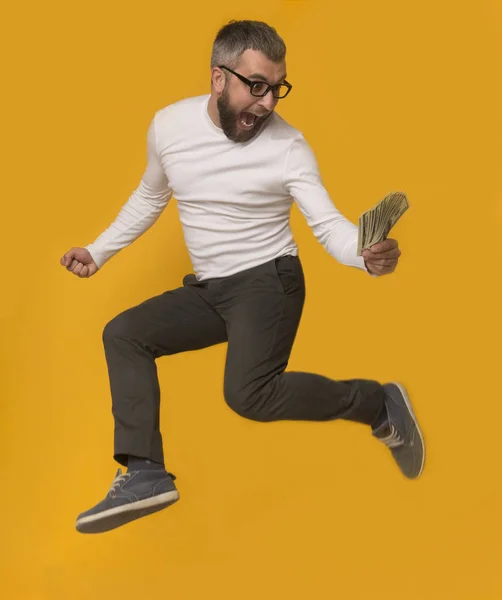 Возбужденный мужчина прыгает с деньгами на желтом фоне — стоковое фото