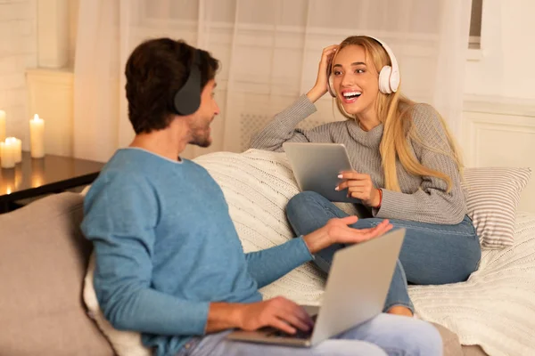 Los cónyuges que utilizan el ordenador portátil y la tableta con auriculares que relajan en casa —  Fotos de Stock