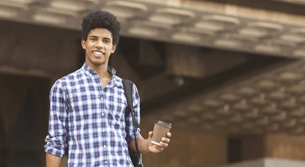 Estudante afro-americano sorrindo para câmera segurando xícara com café — Fotografia de Stock