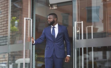 Kendine güvenen Afrikalı işadamı modern ofis merkezinden çıkıyor