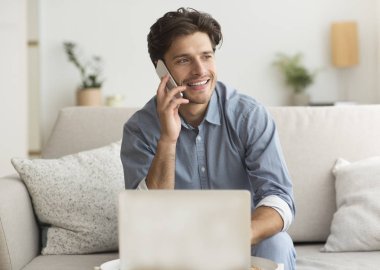 Genç adam içeride dizüstü bilgisayarında oturup keyifli bir telefon görüşmesi yapıyor.