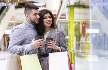 Kahveli mutlu çift dükkan vitrinine bakmaya gidiyor.