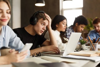 Öğrenci çocuk kütüphanede dizüstü bilgisayar ödevi yapıyor.