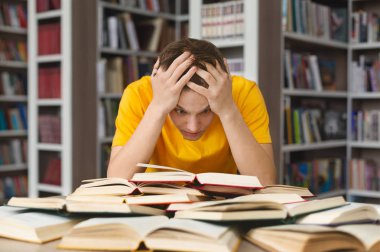 Kafasını tutup kütüphanede kitap okuyan bitkin bir adam.