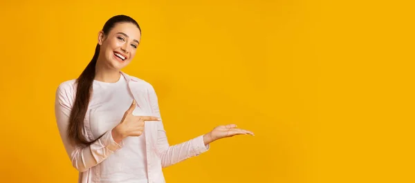 Χαρούμενη κοπέλα που δείχνει το δάχτυλο κρατώντας κάτι στο κίτρινο φόντο — Φωτογραφία Αρχείου