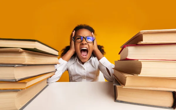 Estudante elementar impressionado gritando embreagem cabeça sentada entre pilhas de livros — Fotografia de Stock