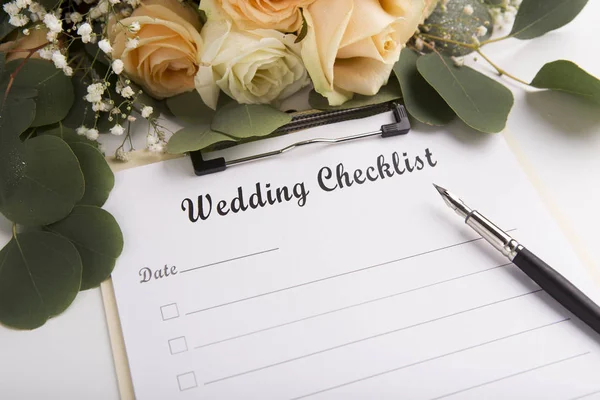 Wedding checklist with creative pen and roses on white table