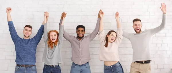 Amis célébrant réussir avec les mains levées sur le mur blanc — Photo