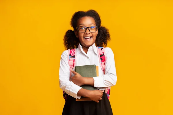 快乐的小学女生拥抱黄色工作室背景的书 — 图库照片