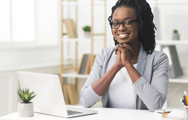 Schwarzes Businessgirl lächelt in die Kamera, die im modernen Büro sitzt — Stockfoto