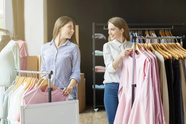 Twee mooie shopaholics glimlachen naar elkaar in de kledingwinkel — Stockfoto