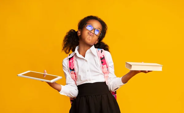 Чорна школярка порівнюючи планшетний комп'ютер і книгу на жовтому тлі — стокове фото
