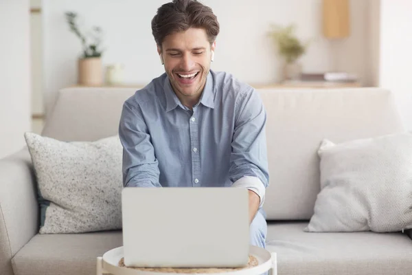 Sonriente chico haciendo videollamada a través de un ordenador portátil sentado en un sofá — Foto de Stock