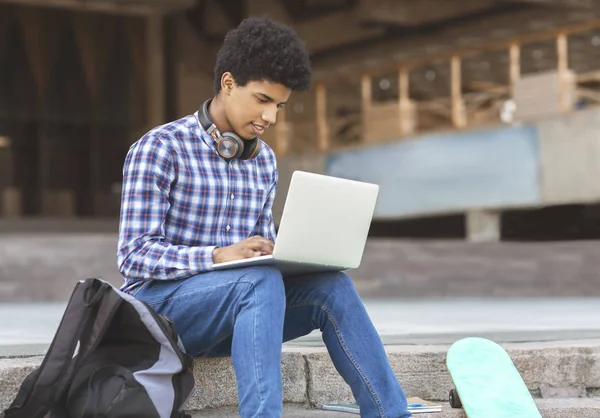 Estudante universitário africano está sentado lá fora, digitando em um laptop — Fotografia de Stock