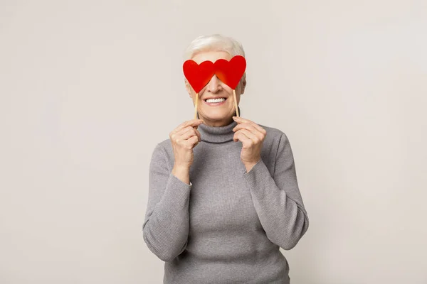 Веселая пожилая женщина с красными бумажными сердцами, закрывающими глаза — стоковое фото