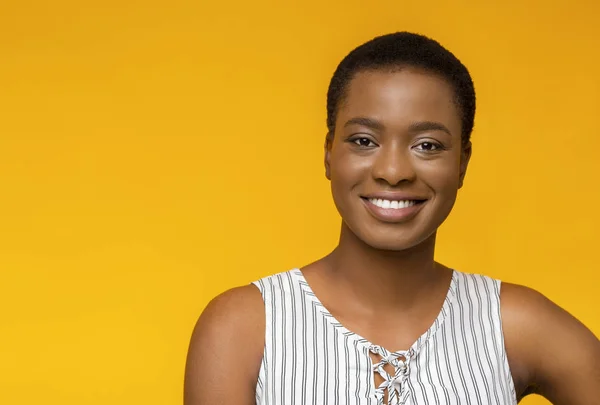 Aantrekkelijk zwart meisje glimlachend op gele studio achtergrond — Stockfoto