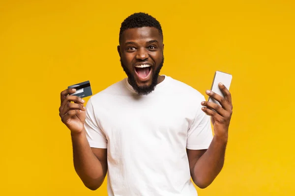 Homem africano feliz segurando cartão de crédito e celular em suas mãos — Fotografia de Stock