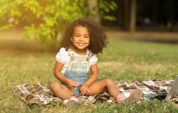Słodkie afrykańsko-amerykańska dziewczyna siedzi na kocu na trawie — Zdjęcie stockowe