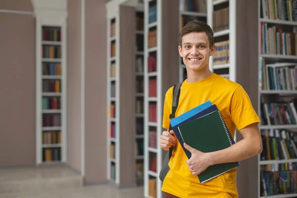 Возбужденный студент-мужчина позирует рядом с книжными полками в библиотеке — стоковое фото