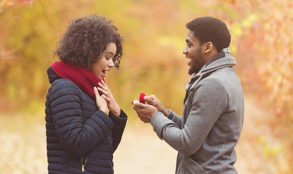 Romantic afro man proposing to woman in autumn park