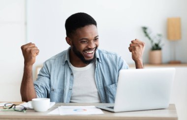 Afro işadamı başarıyı kollarını kaldırıp dizüstü bilgisayara bakarak kutluyor