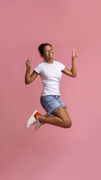 Cute african american girl jumping and showing peace sign — Stock Photo, Image