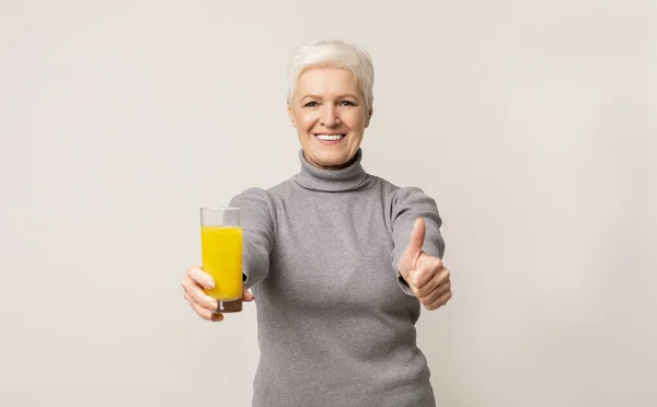 Старшая женщина рекомендует апельсиновый сок, показывая большой палец на камеру — стоковое фото