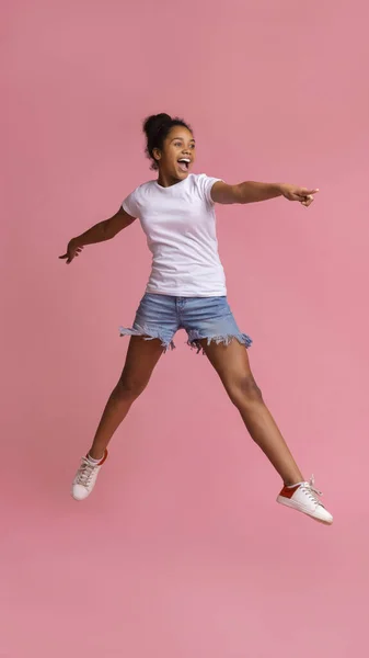 Spójrz tam. Podekscytowana afrykańska dziewczyna skacze i wskazuje na bok — Zdjęcie stockowe