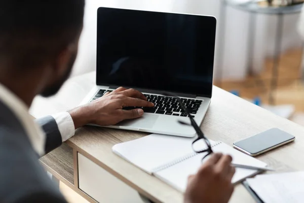 Uomo d'affari nero che lavora sul computer portatile sul suo posto di lavoro — Foto Stock