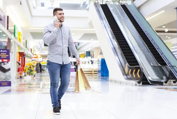 Handsome man with shopping bags talking on phone in mall — Stock Photo, Image