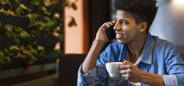 A fekete fickó mobilon beszél és mosolyog a kávézóban. — Stock Fotó