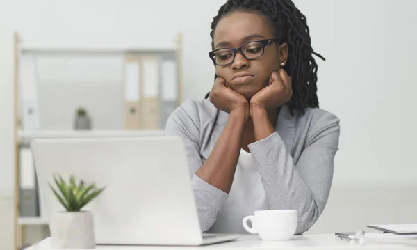 Θλιβερή μαύρη επιχειρηματίας κάθεται στο φορητό υπολογιστή αγγίζοντας πηγούνι στο γραφείο — Φωτογραφία Αρχείου
