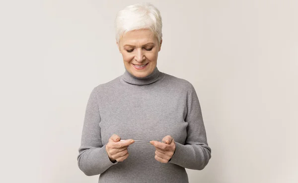 Старшая женщина играет в видеоигры на мобильном телефоне и улыбается — стоковое фото