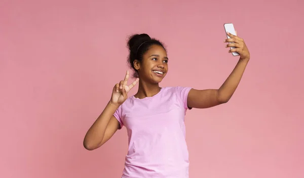 Neşeli Afrikalı kız akıllı telefondan selfie çekiyor, barış jesti gösteriyor. — Stok fotoğraf