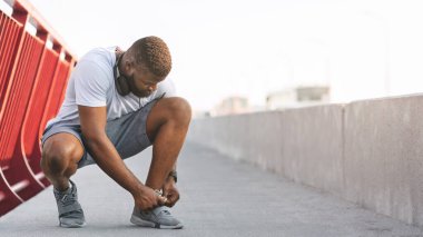 Köprüdeki ayakkabı bağcıklarını kontrol eden afro adam.