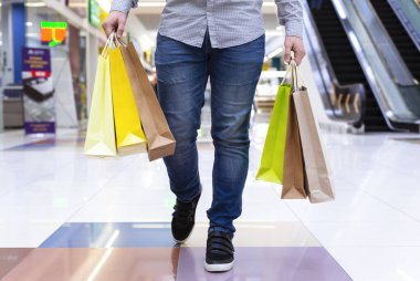 Alışveriş merkezinde alışveriş torbalarıyla yürüyen genç adam.
